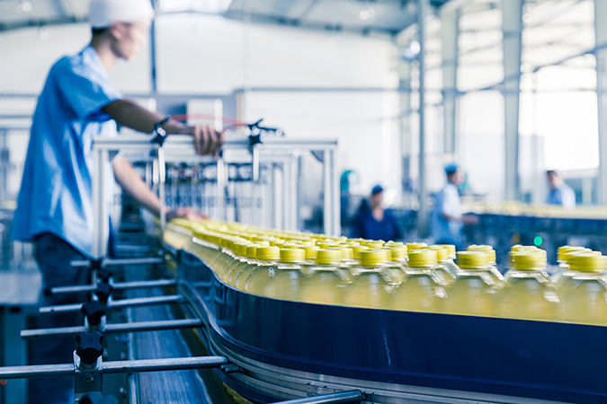 factory worker overseeing yellow-capped bottles on a conveyor belt