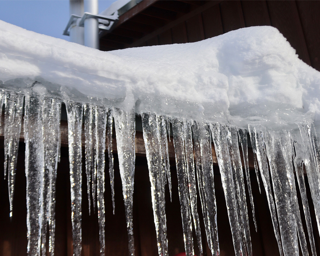 clear icicles hanging from a snow-covered roof during winter, showcasing seasonal weather and frozen water formations