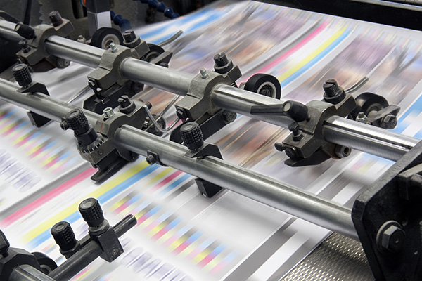 close-up of a printing press in operation with colorful printed sheets moving through rollers and mechanical components
