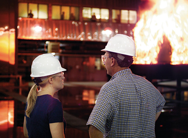 two people in hard hats observing a large industrial fire near a lit building